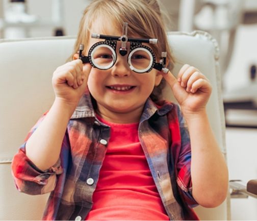 Ein Kind mit Kopfhörern sitzt auf einem modernen Stuhl, hält die Ohrstöpsel und blickt in die Kamera in einer hellen, luftigen Umgebung.