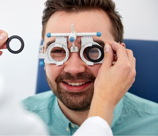 Eine medizinische Fachkraft führt eine Augenuntersuchung mit einem schwarzen Ringgerät in der Nähe eines Patienten durch, der in einer klinischen Umgebung sitzt.